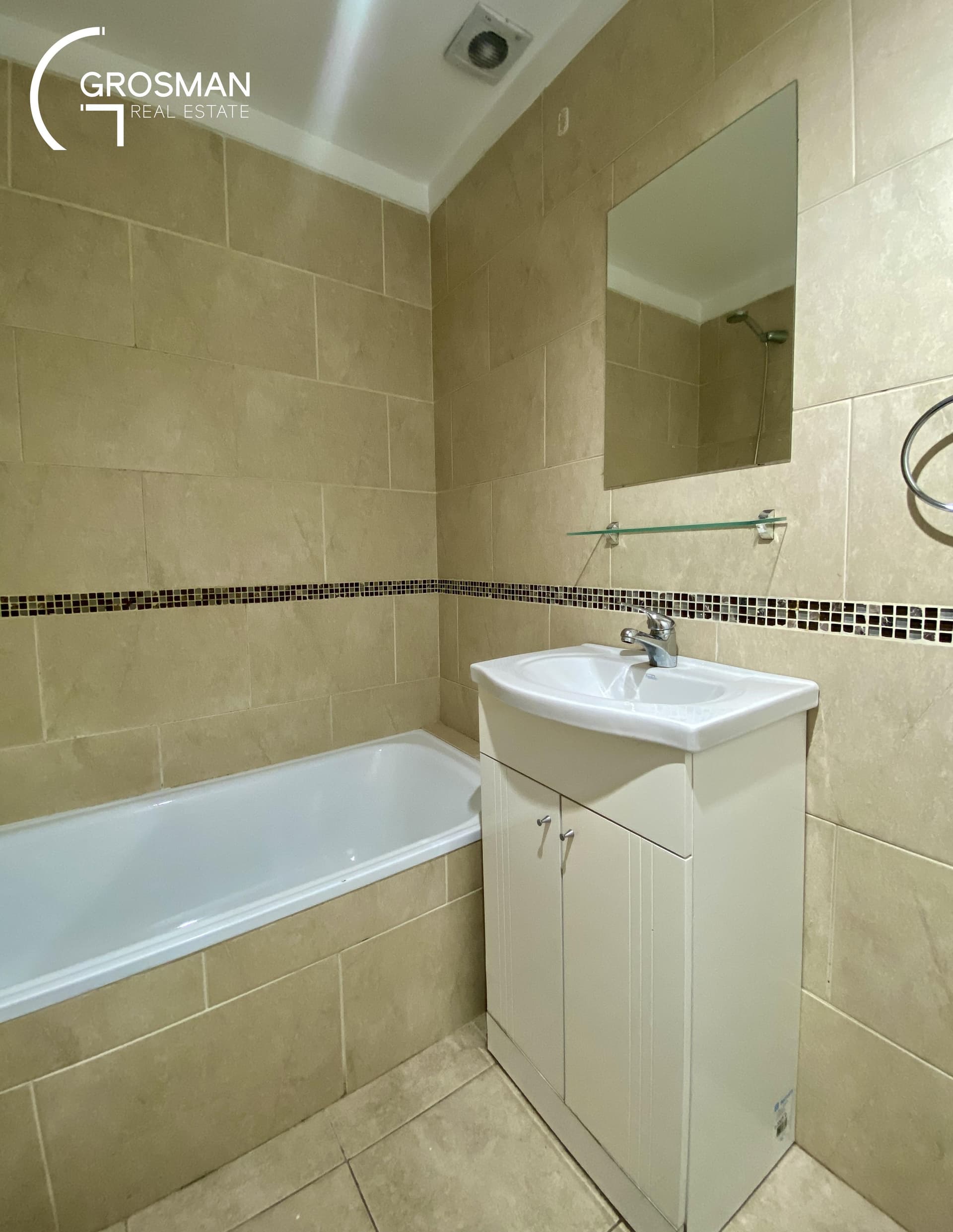 Baño con bañera, vanitory y espejo, azulejos claros con guarda.