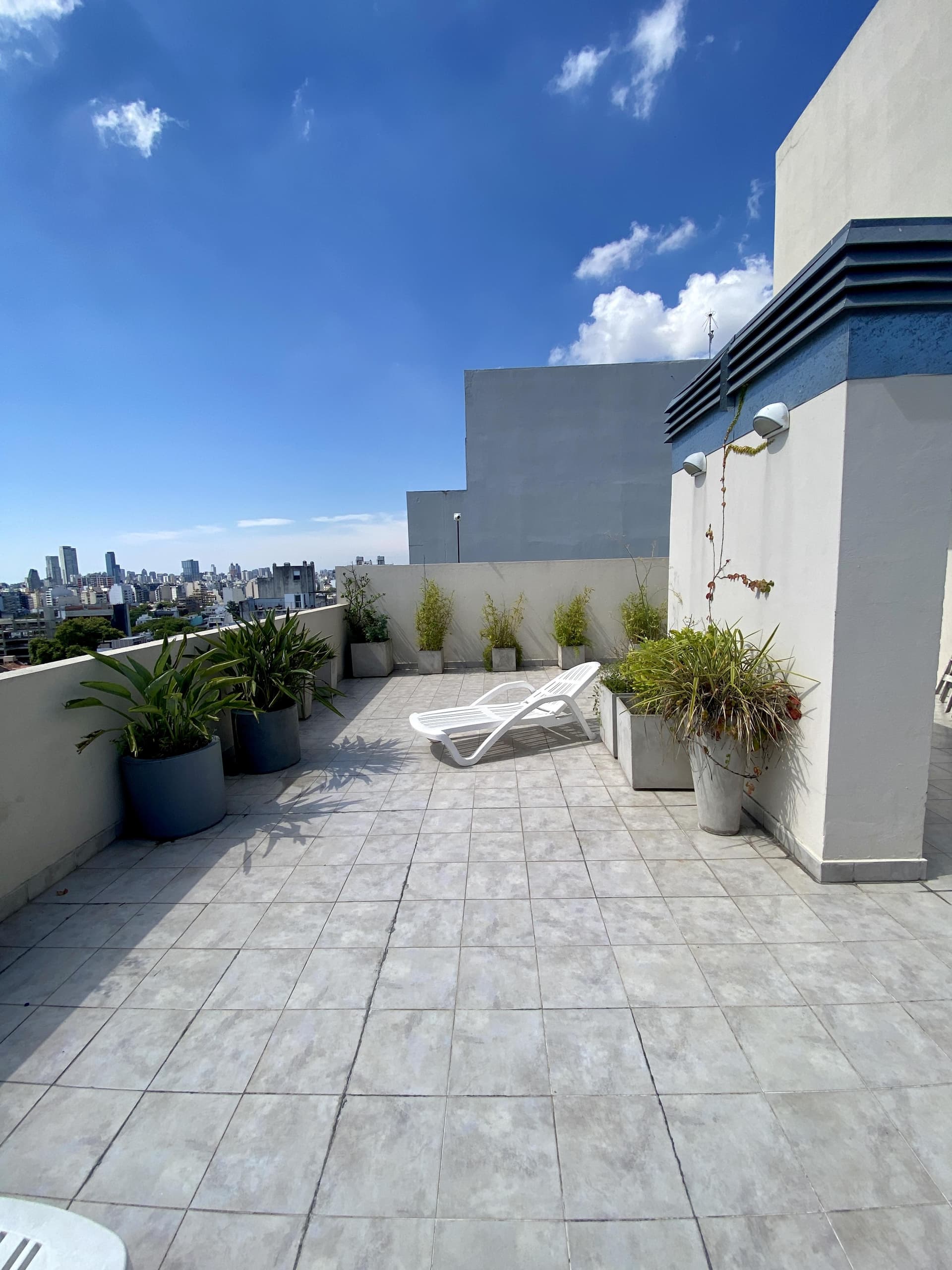 Terraza amplia con una reposera y plantas, con vista a la ciudad.