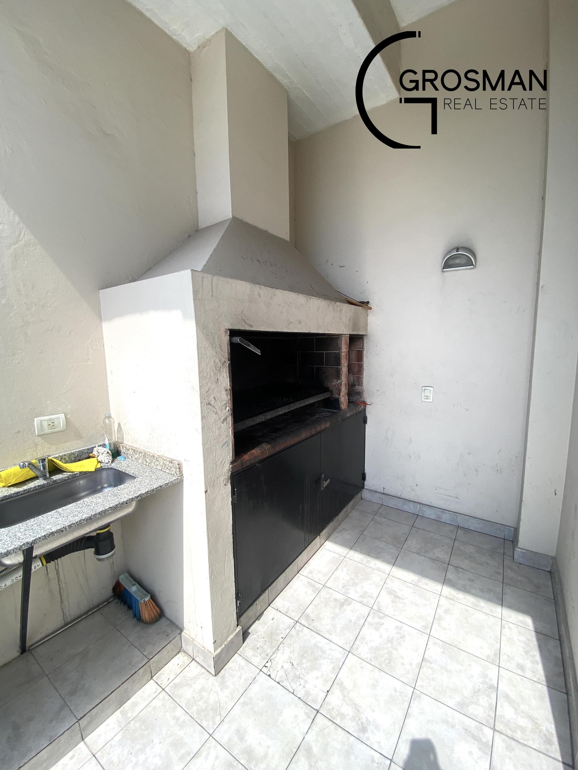 Parrilla con campana, bacha y mesada en un espacio común.