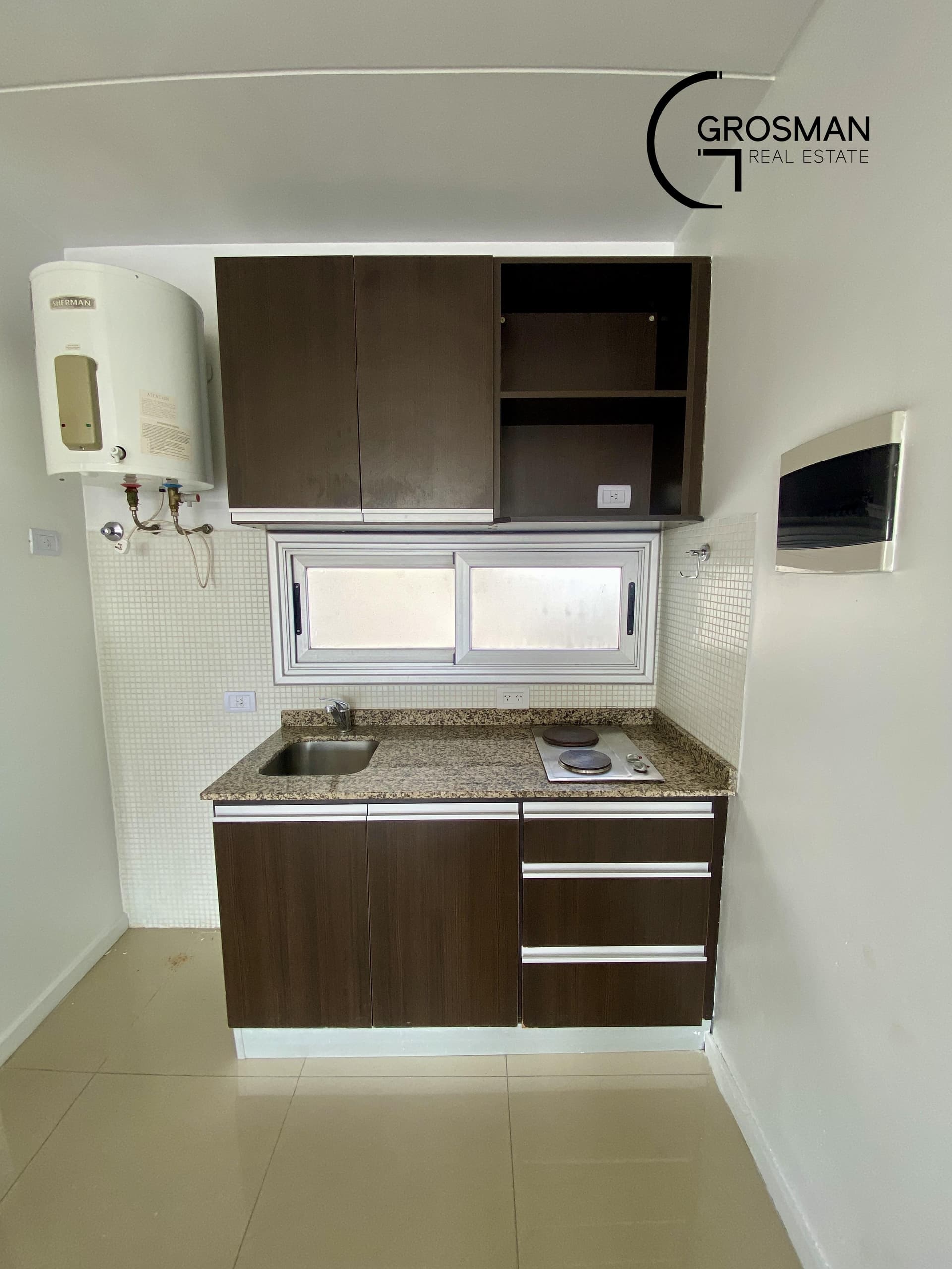 Cocina con mesada de granito, anafe, bacha y alacenas marrones.