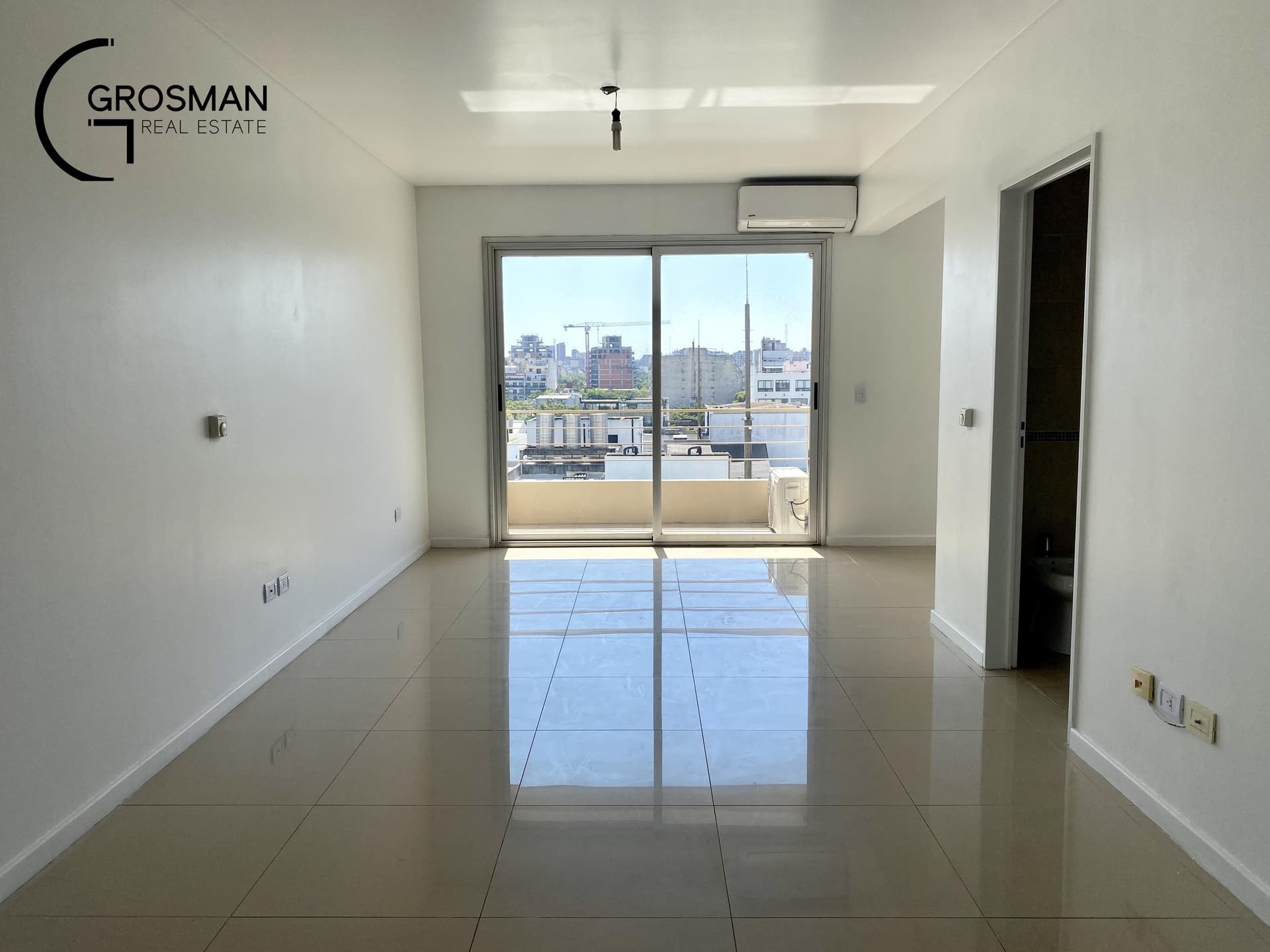 Living vacío con puerta balcón y vista a la ciudad.