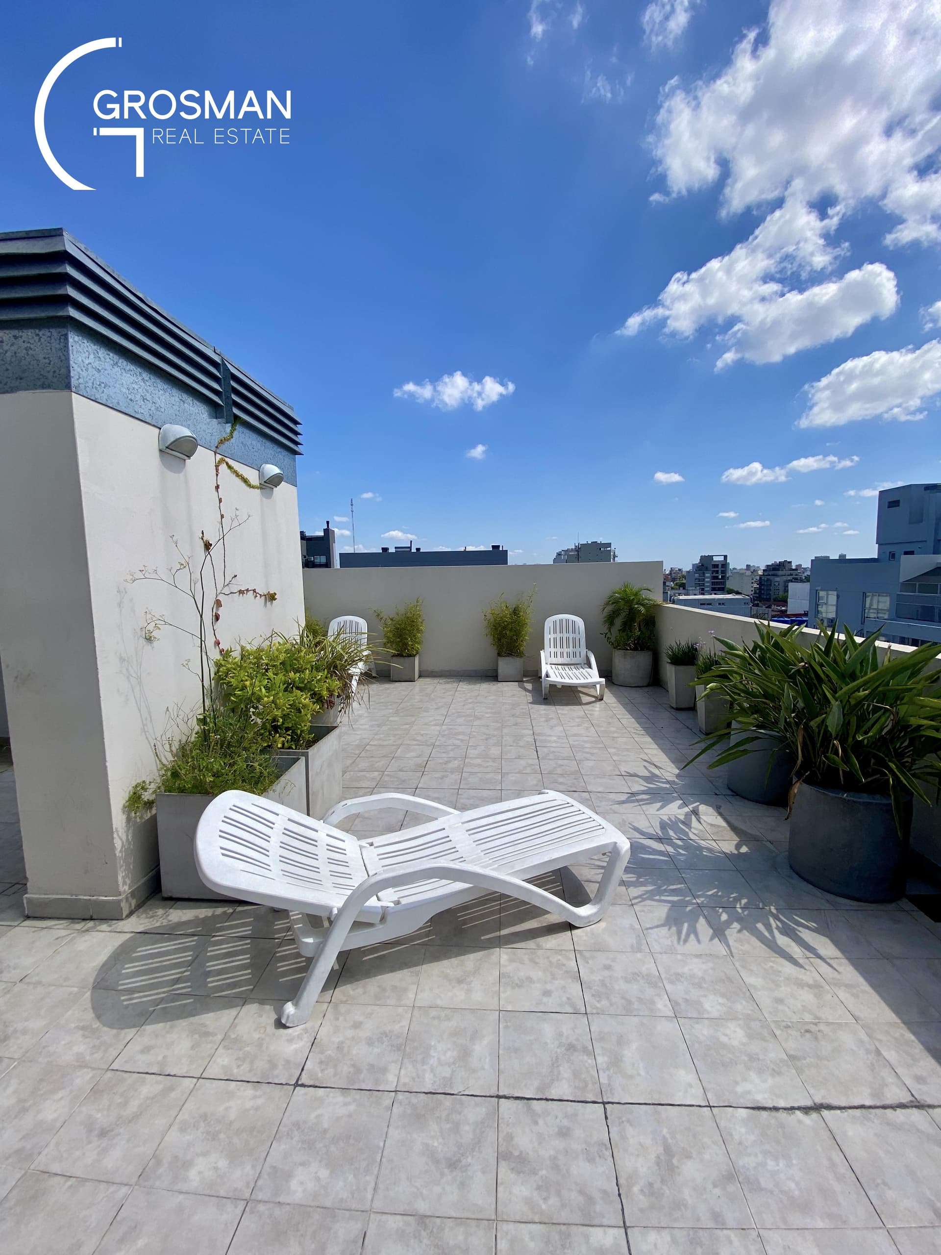 Terraza con reposeras blancas, plantas en macetas y cielo azul.