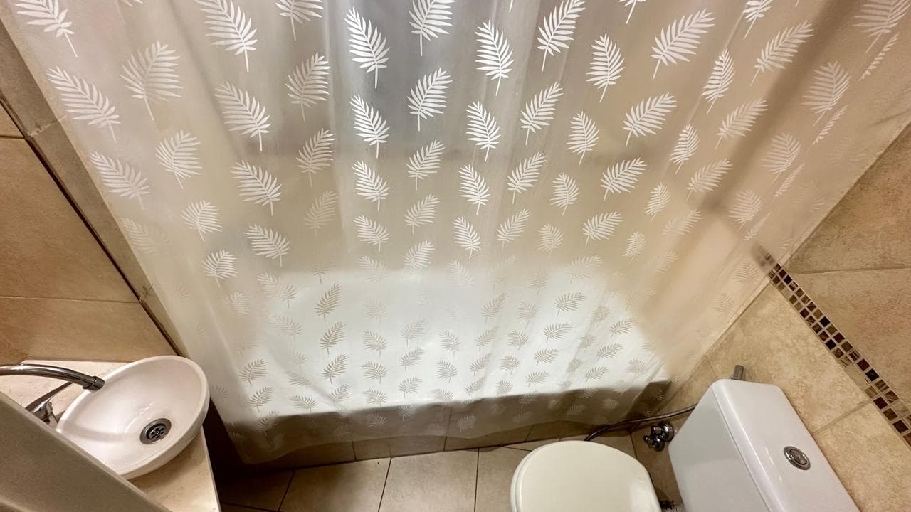 Baño completo con inodoro, lavatorio y bañera con cortina de ducha.