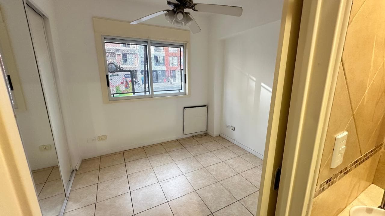 Dormitorio vacío con ventana, piso de baldosas y placard con espejo.