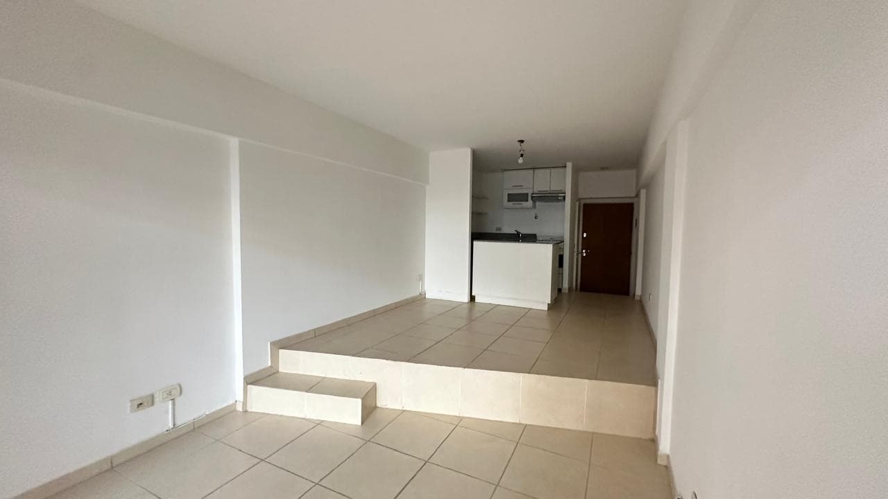 Living amplio con desnivel, piso de baldosas y cocina integrada al fondo.