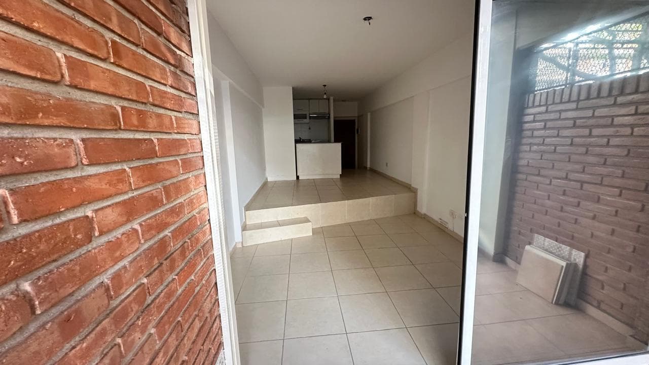 Balcón con pared de ladrillo, rejas y vista al living interior.