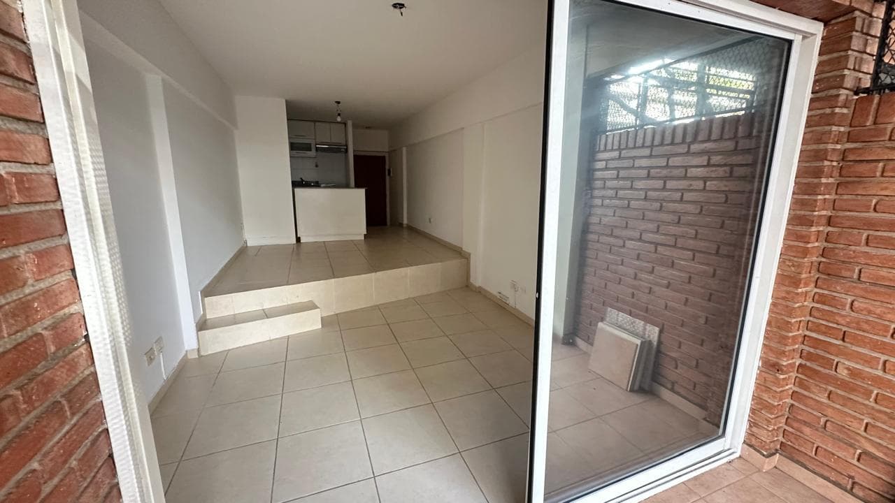 Balcón con pared de ladrillo, rejas y vista al interior del departamento.