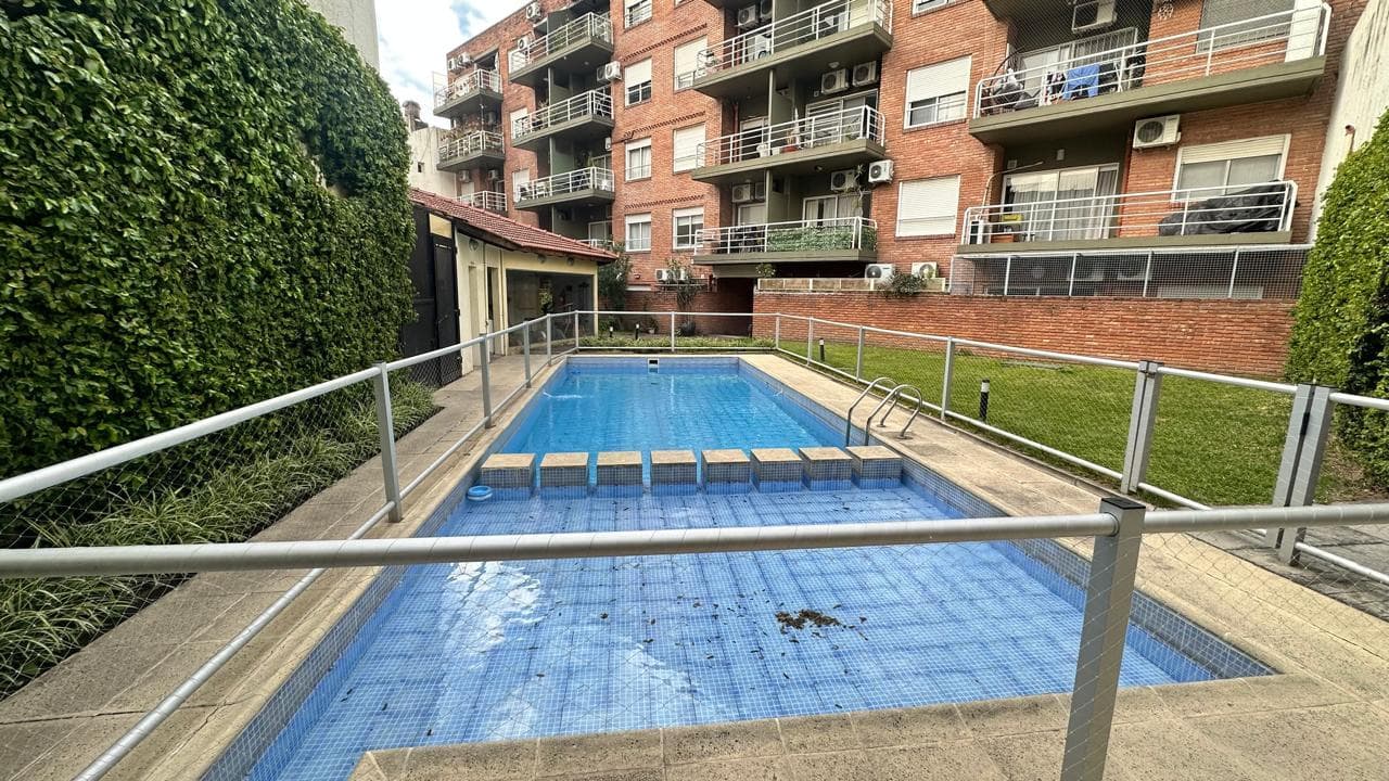 Pileta exterior del edificio con cerco de seguridad y vegetación.
