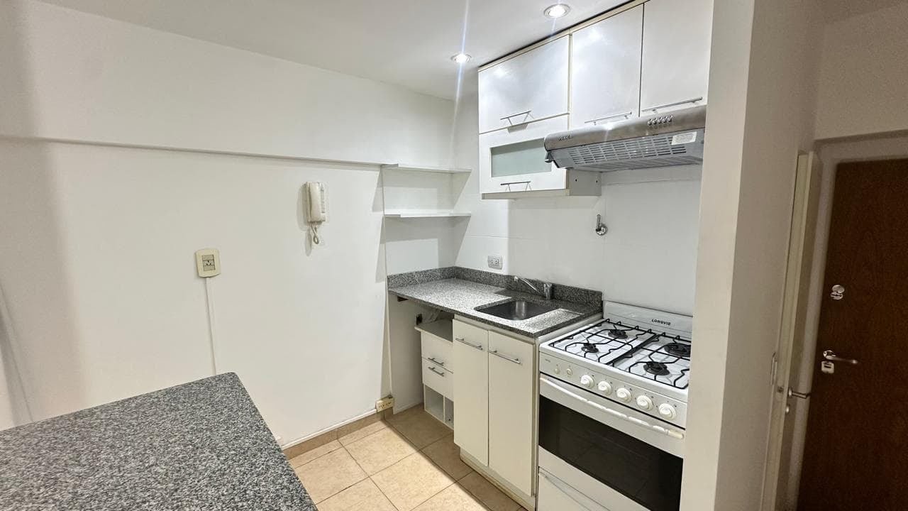 Cocina con mesada de granito, bacha, anafe, horno y alacenas blancas.
