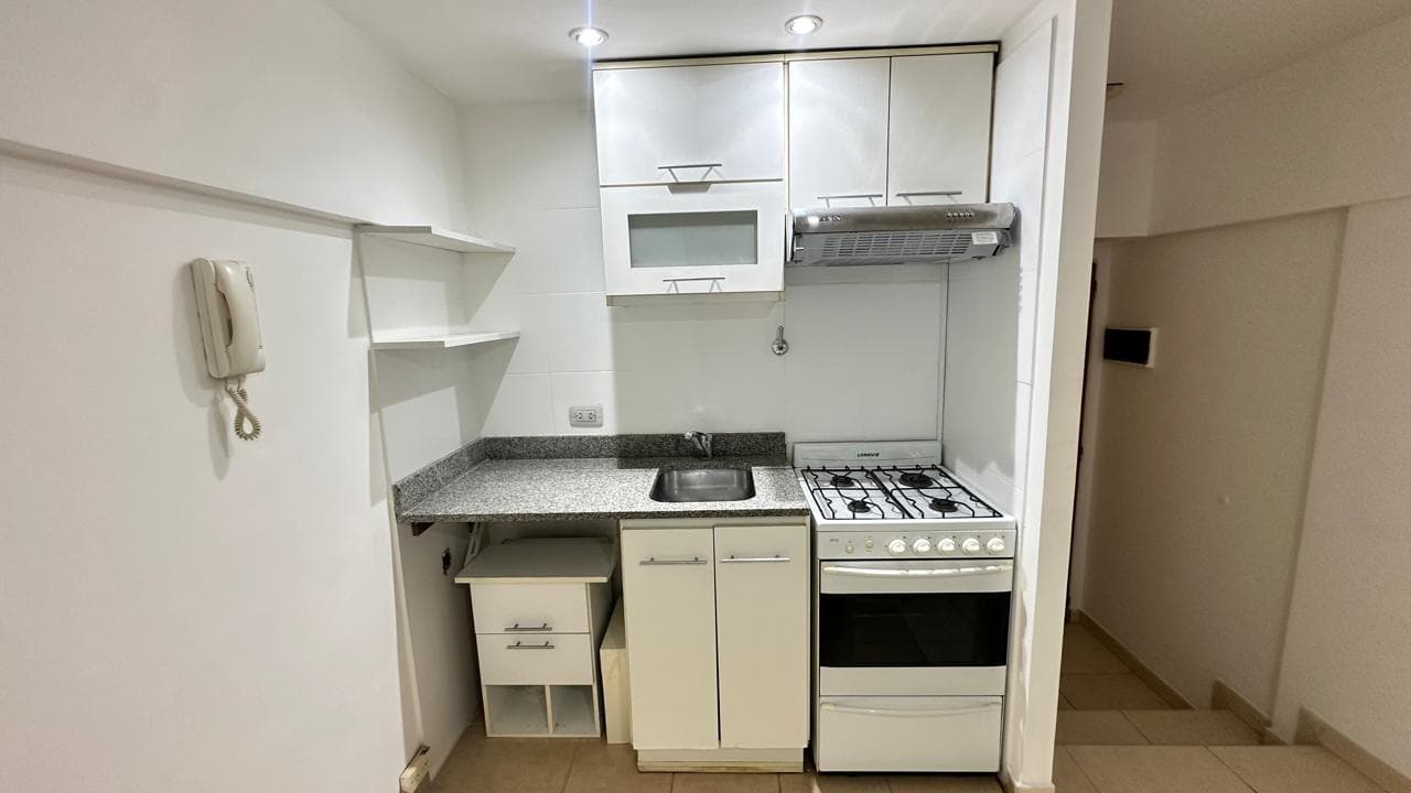 Cocina con mesada, bacha, anafe, horno y alacenas blancas modernas.