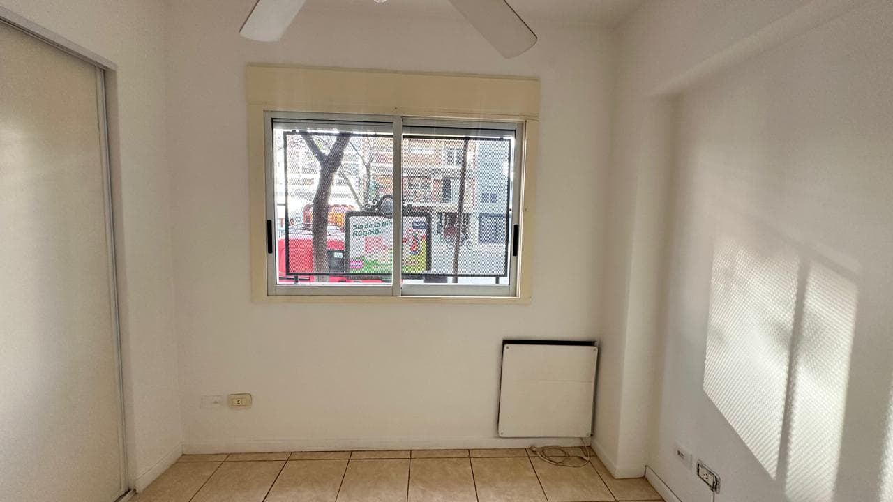 Dormitorio vacío con ventana grande, piso de baldosas y ventilador.