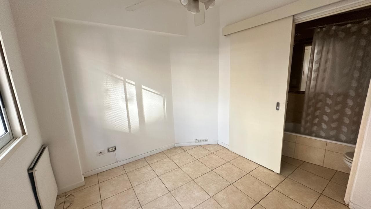 Dormitorio vacío con ventana, ventilador de techo y puerta al baño.