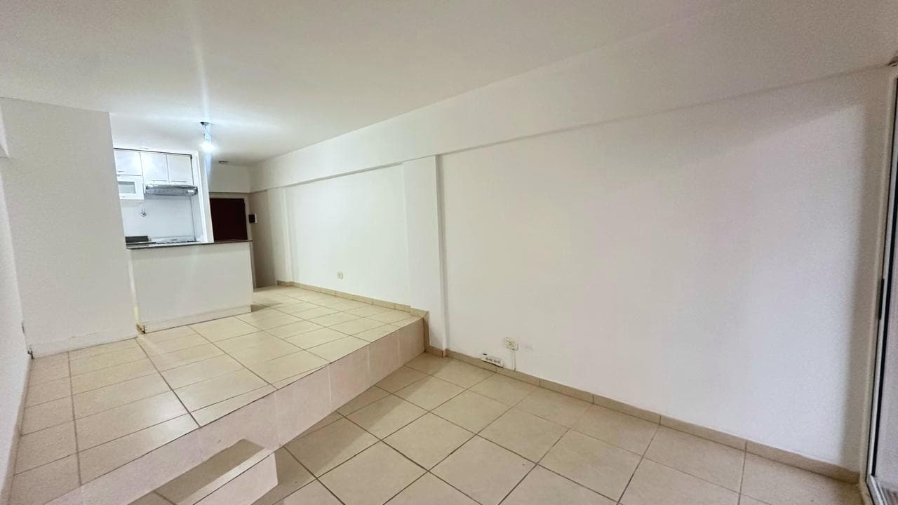 Living amplio con desnivel, piso de baldosas y vista hacia la cocina.