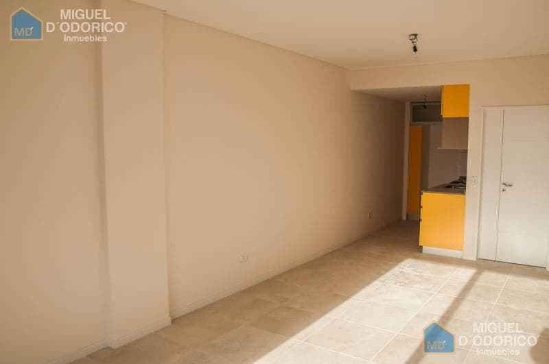 Living vacío con cocina integrada de muebles amarillos al fondo.
