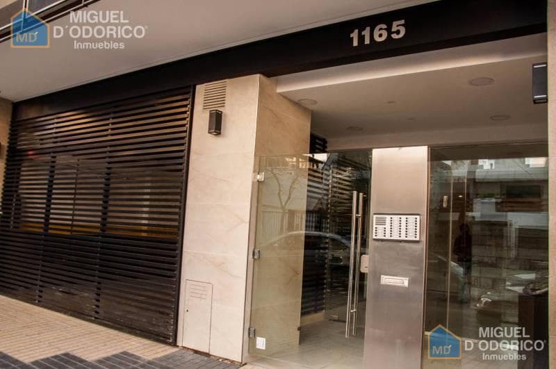 Entrada del edificio con puerta de vidrio, rejas y número 1165.
