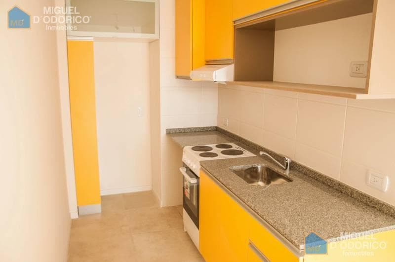 Cocina con mesada de granito, bacha, anafe eléctrico y alacenas amarillas.