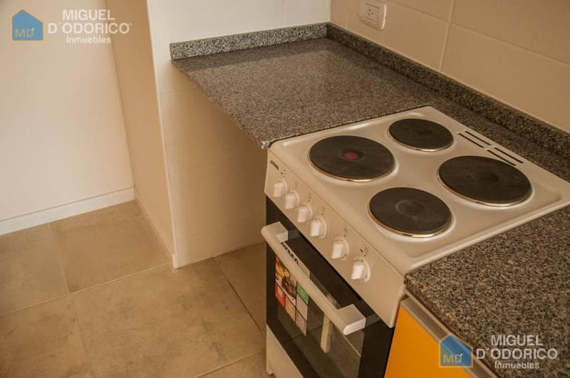 Detalle de cocina con anafe eléctrico, horno y mesada de granito.