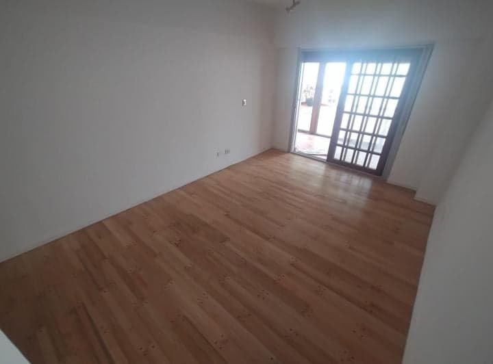 Dormitorio vacío con piso de madera claro y puerta de vidrio al exterior.