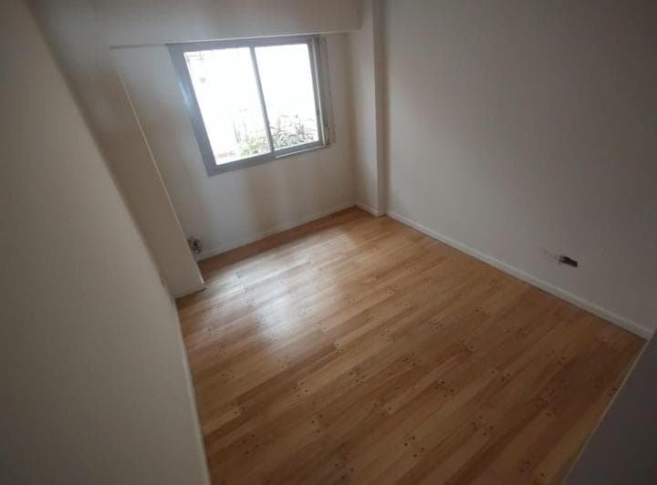 Dormitorio vacío con piso de madera y ventana con rejas.
