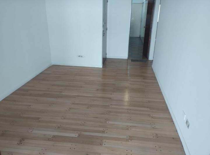 Living vacío con piso de madera y vista a un pasillo interior.