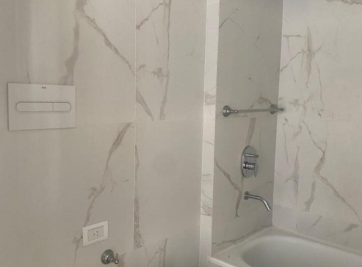 Baño con inodoro, azulejos de mármol y bañera con grifería.