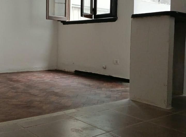 Living vacío con piso de parquet, ventana abierta y paredes blancas.