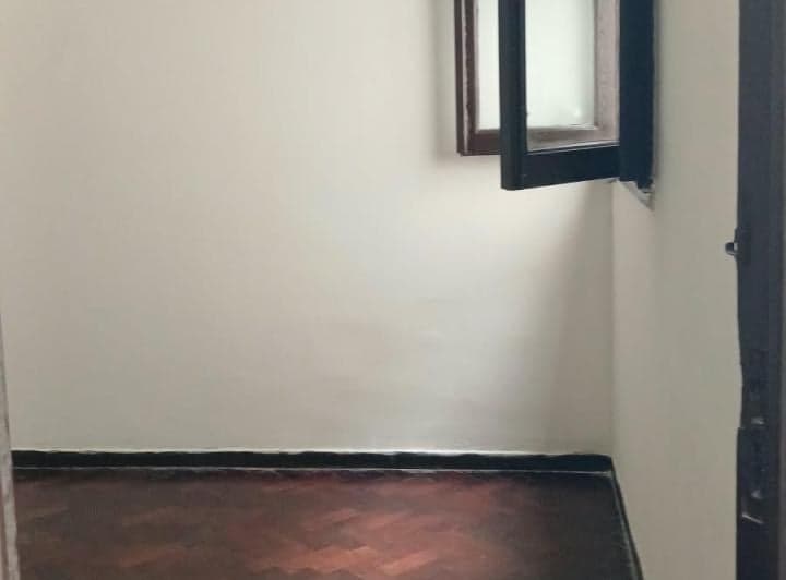 Dormitorio vacío con piso de parquet y ventana con marco oscuro.