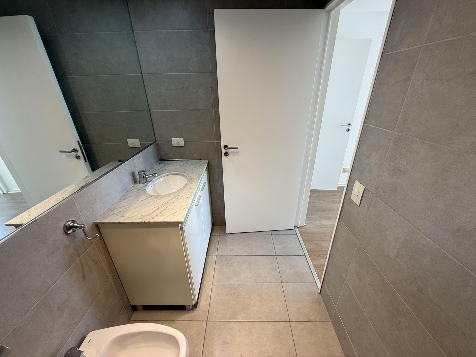 Toilette con vanitory, bidet, inodoro y gran espejo en la pared.