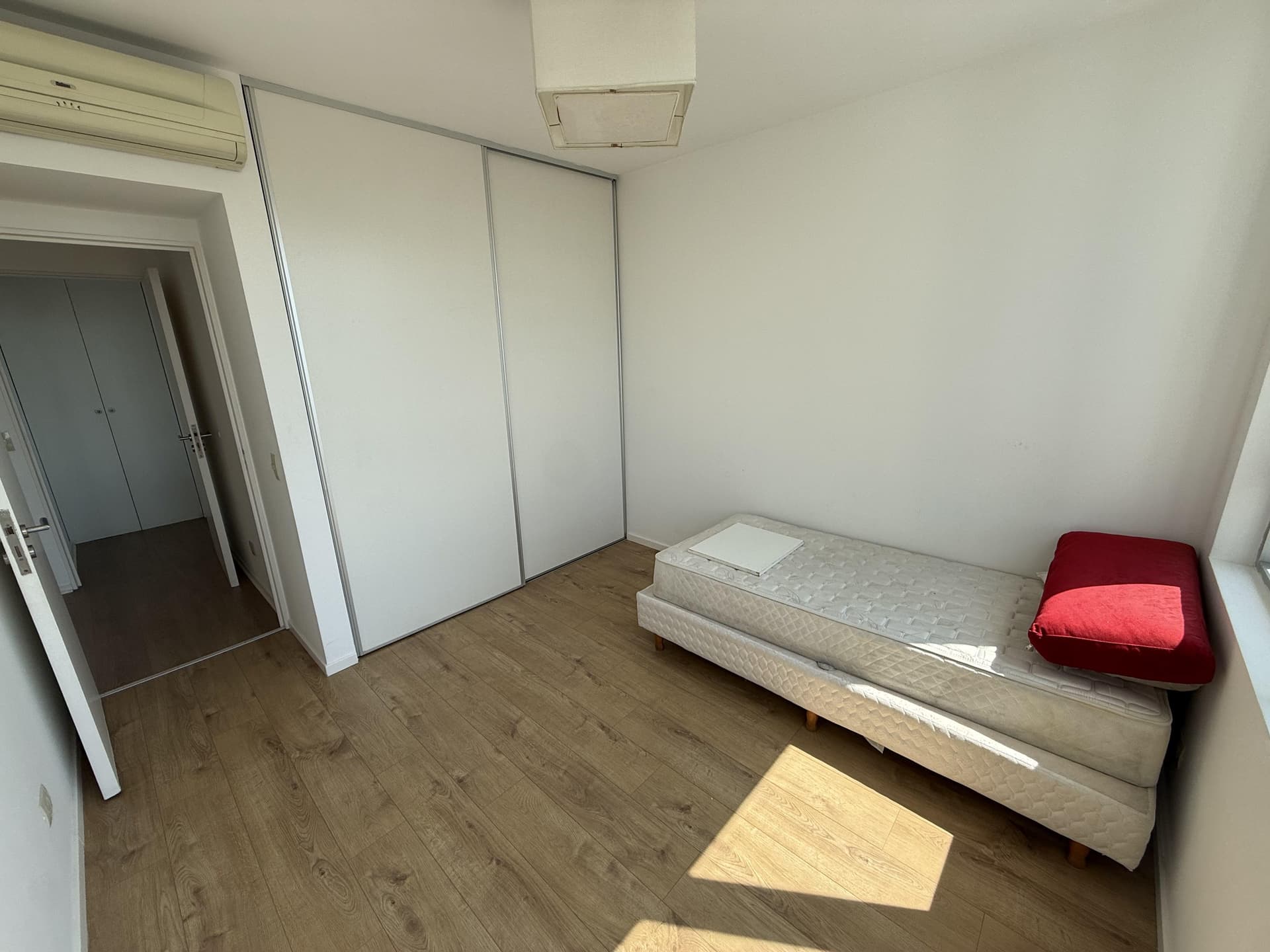 Dormitorio con cama individual, placard de puertas corredizas y aire acondicionado.