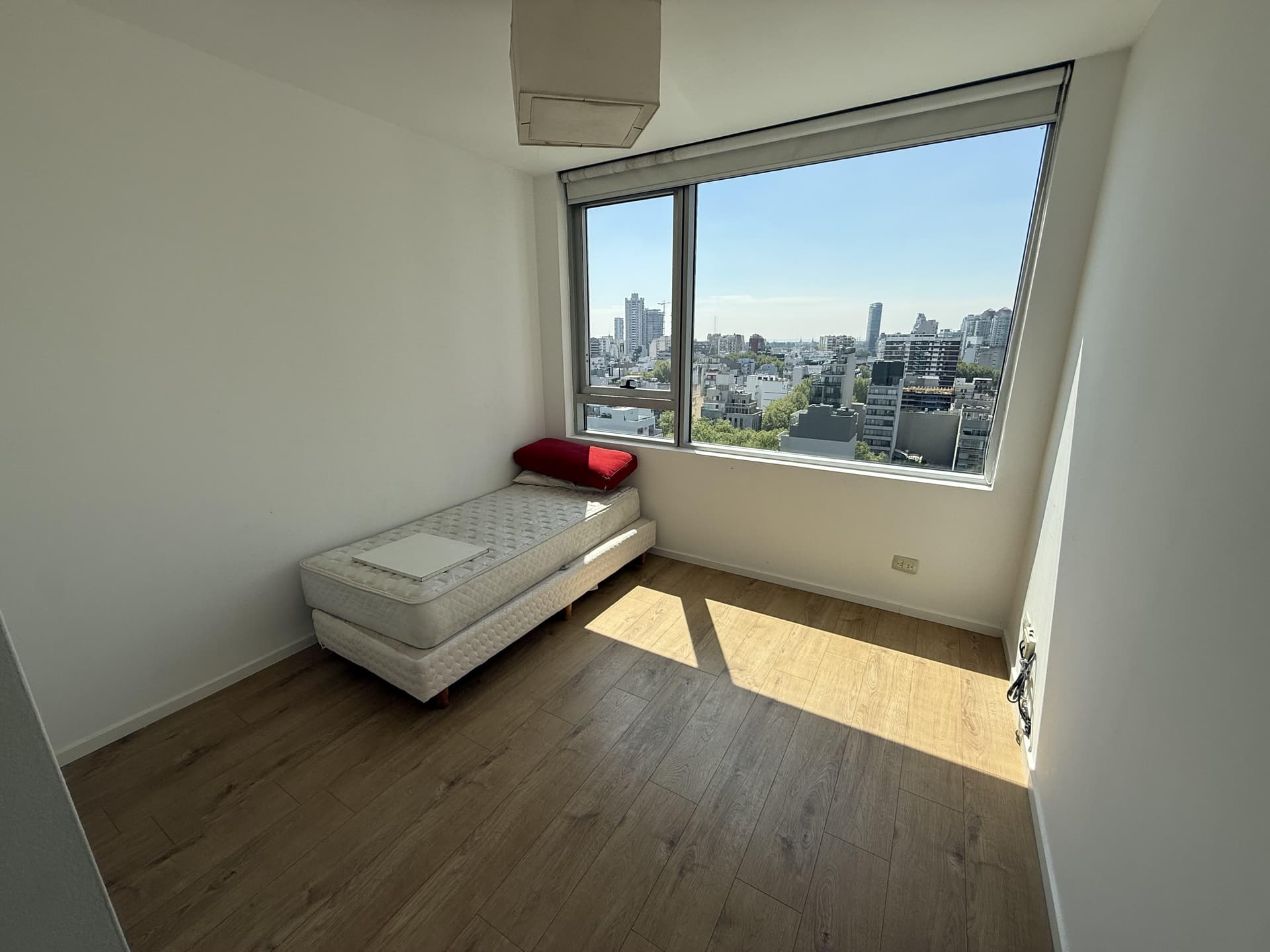 Dormitorio con cama individual y amplio ventanal con vista a la ciudad.