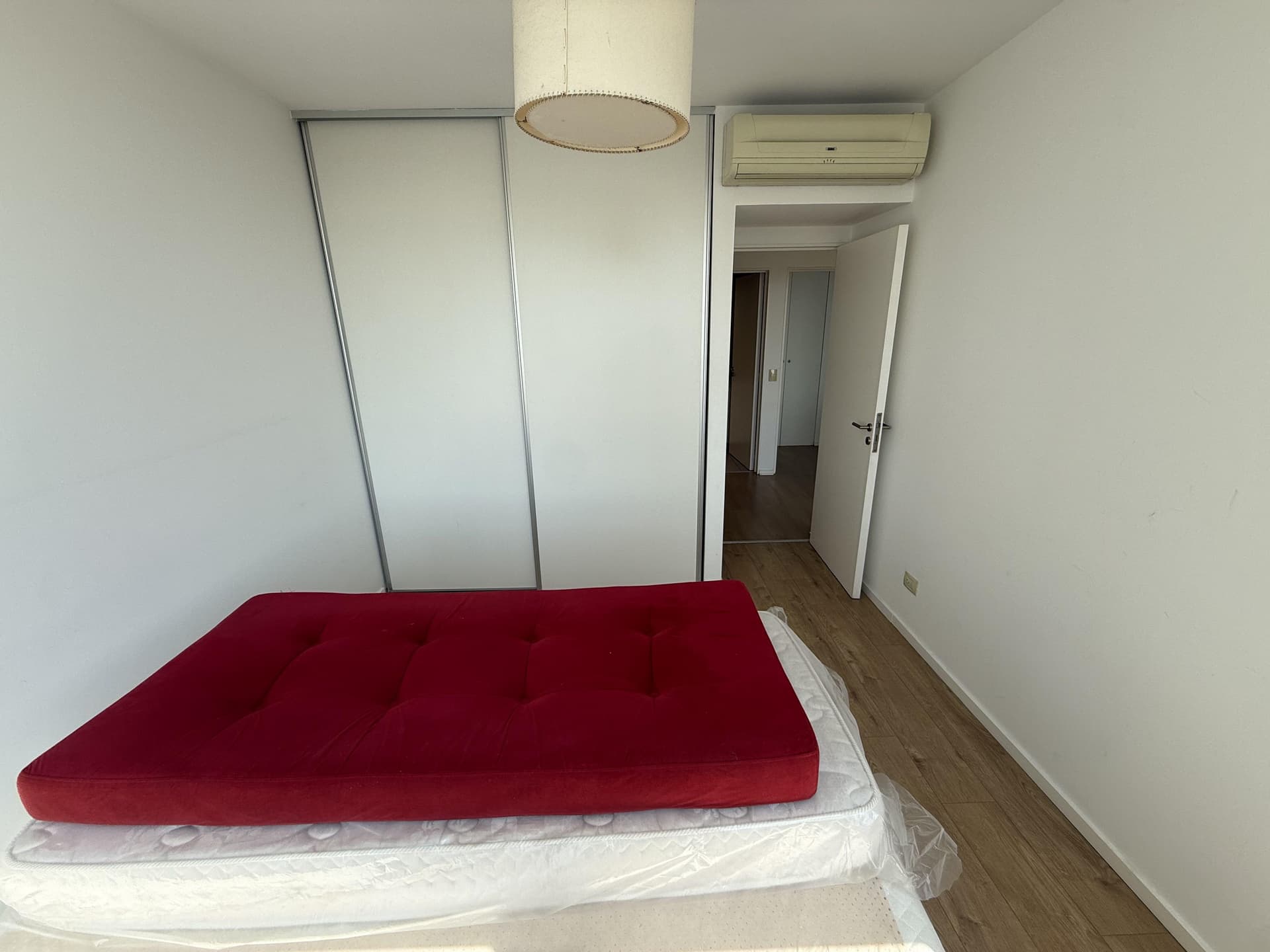 Dormitorio con cama roja, placard blanco y aire acondicionado.