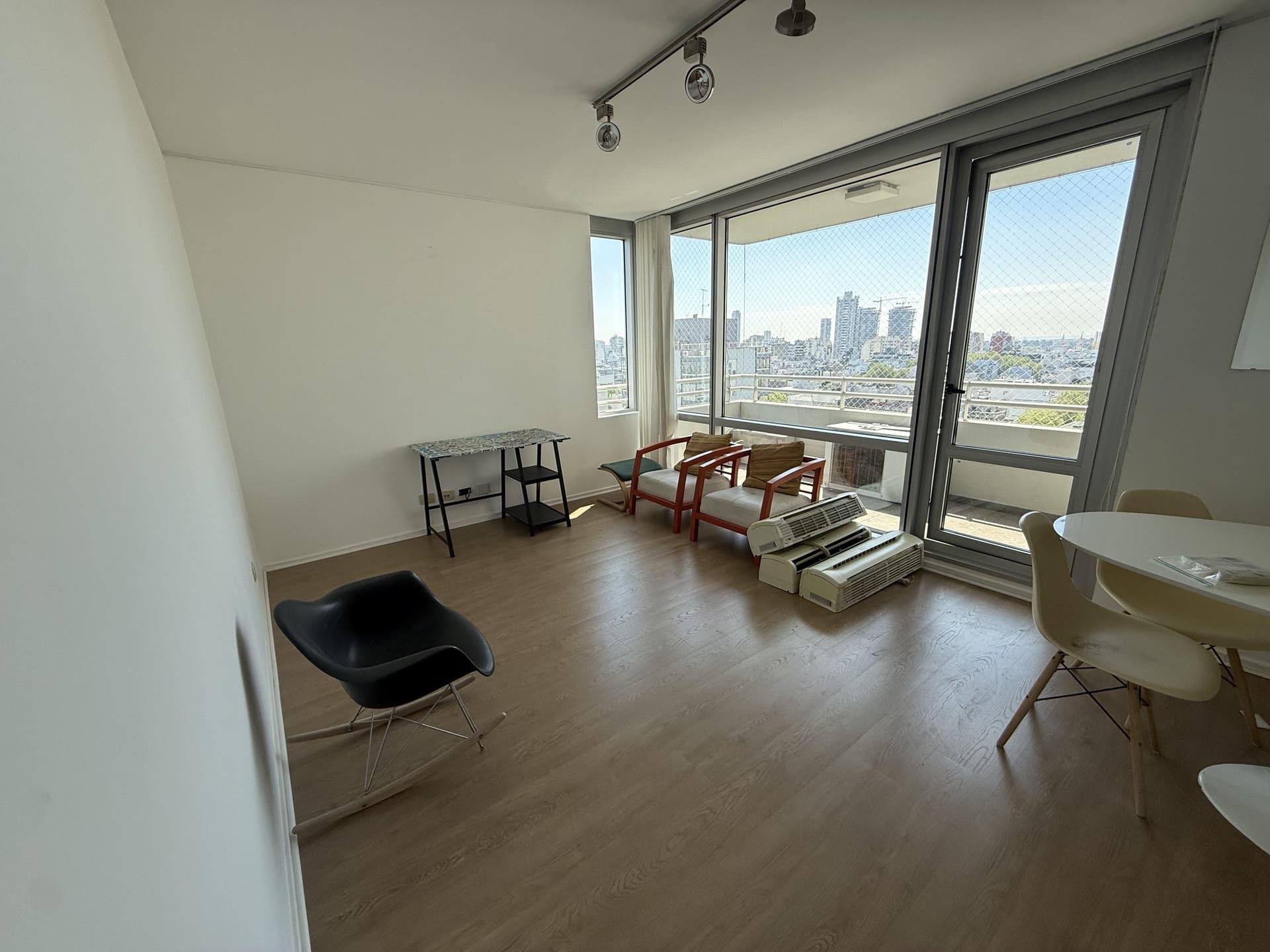 Living con sillones, sillón mecedor y amplio ventanal con vista a la ciudad.
