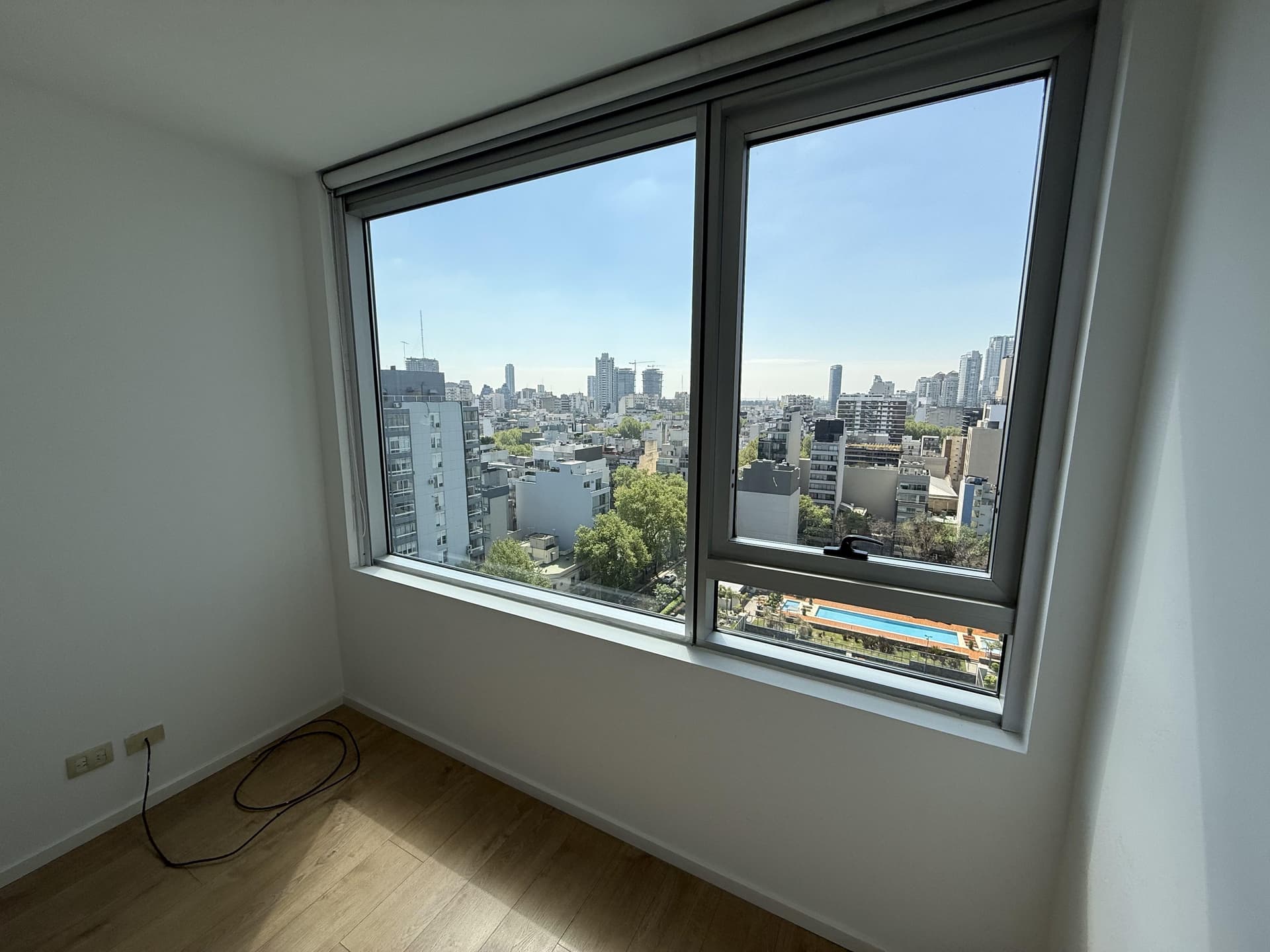 Ventana con vista a la ciudad y piscinas de un complejo cercano.