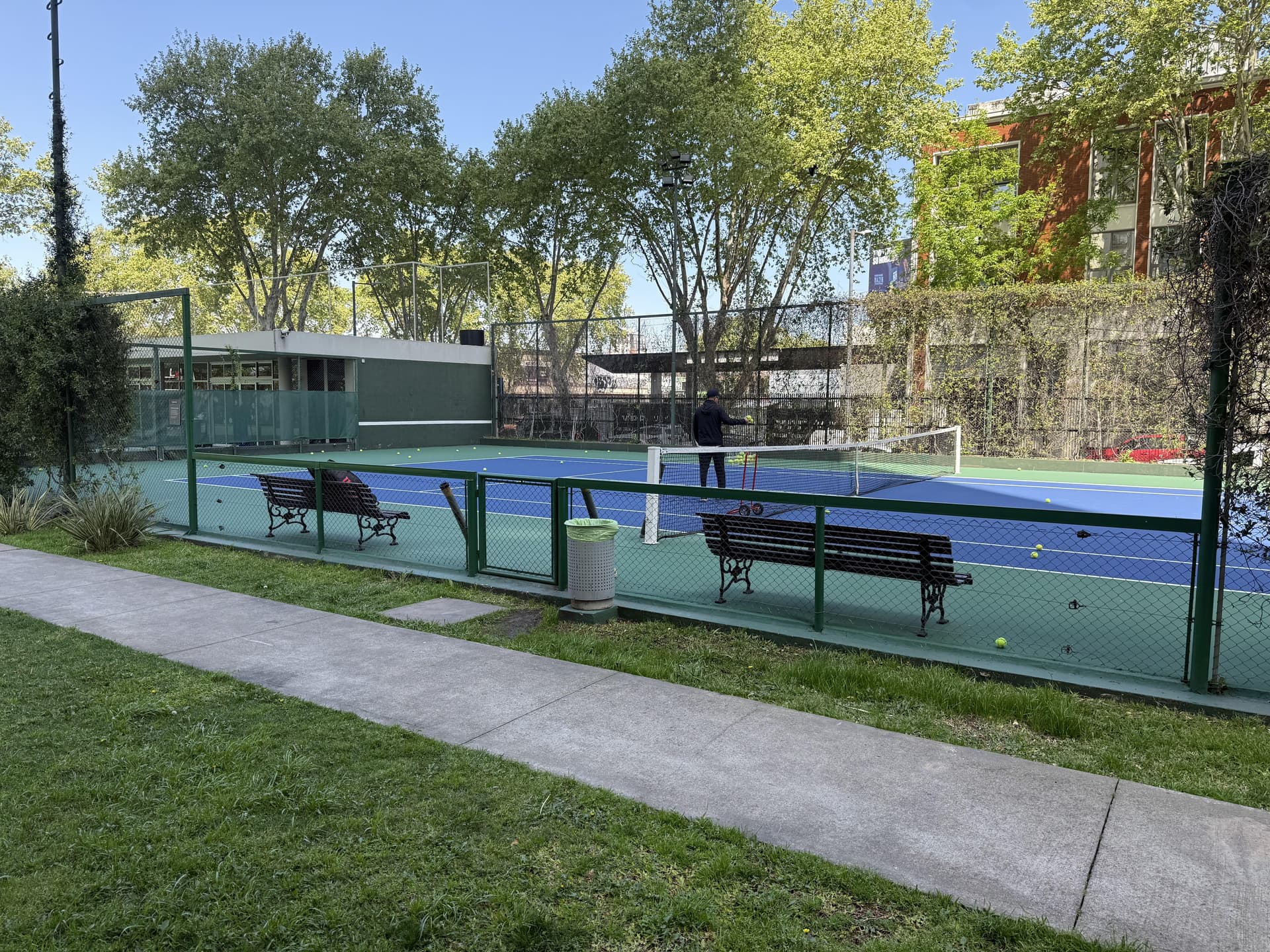 Cancha de tenis con jugadores y bancos de descanso alrededor.