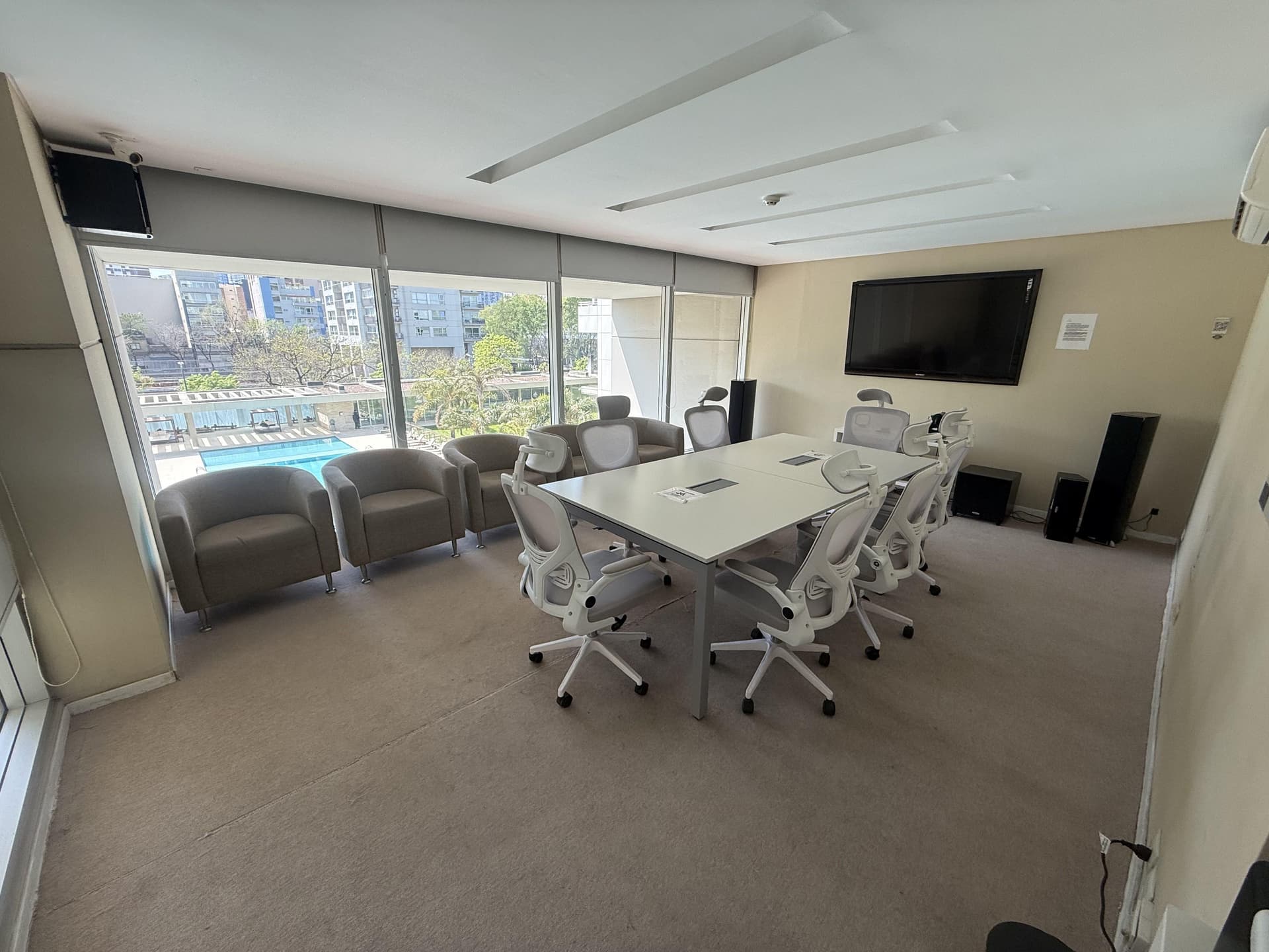 Sala de reuniones con mesa central, sillas y sillones, con vista a la piscina.