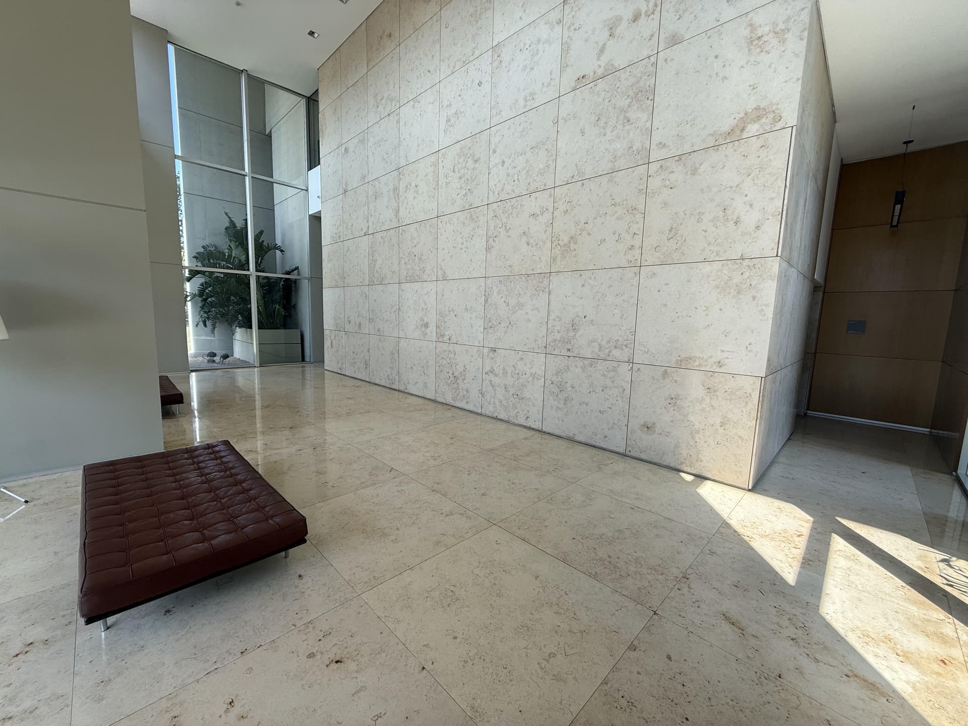 Hall de entrada de un edificio con paredes de piedra y ventanales altos.