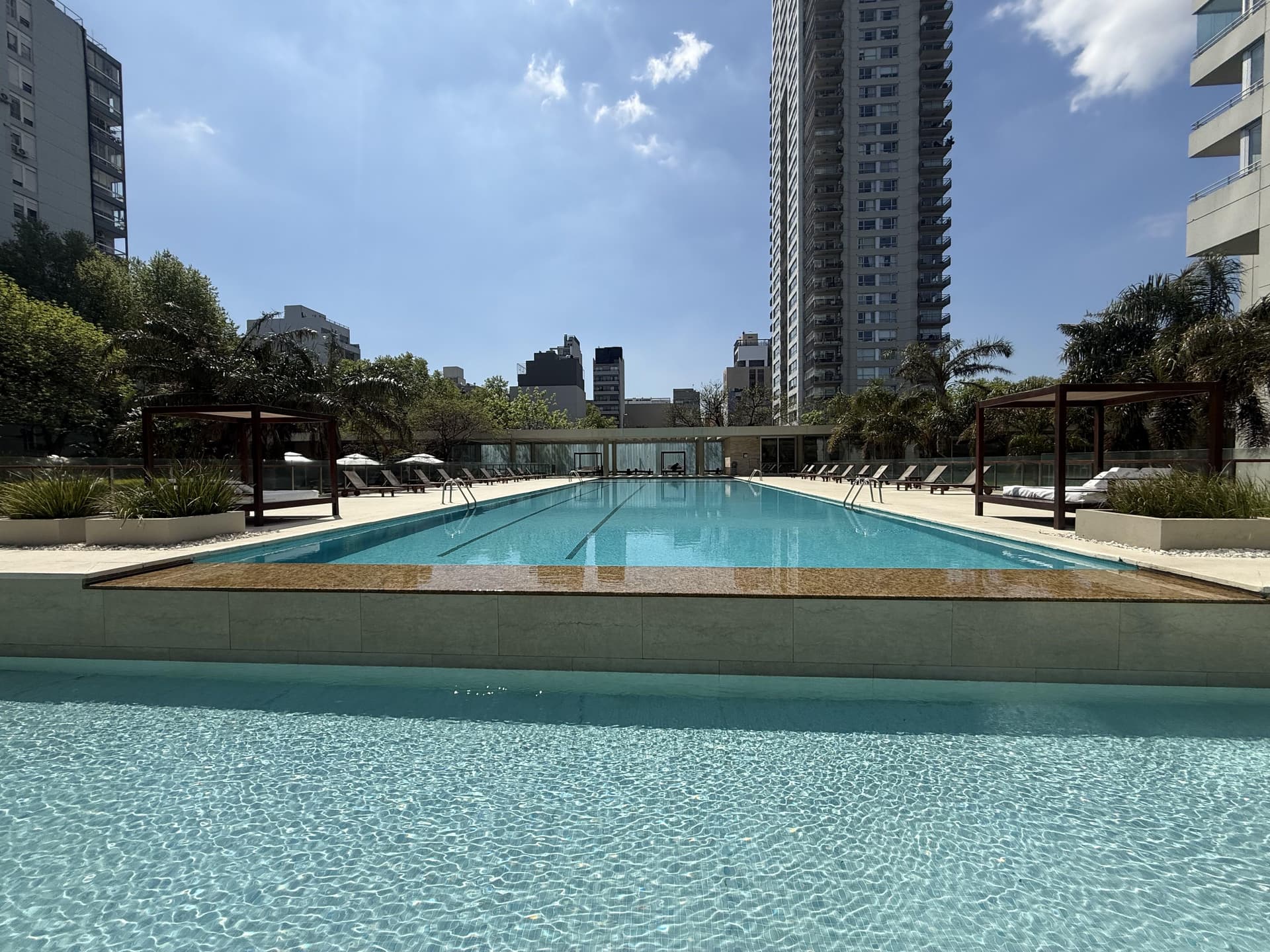 Piscina de gran tamaño con reposeras y sombrillas en un día soleado.