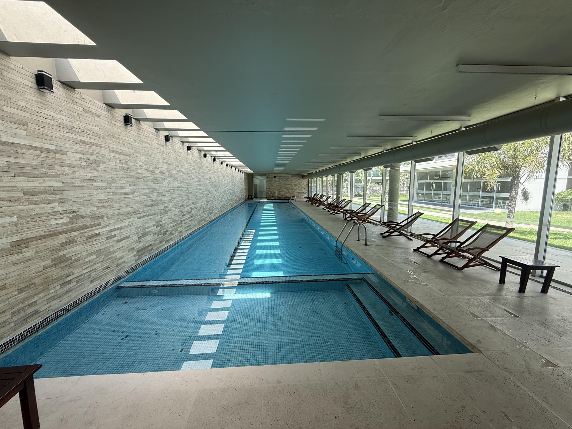 Piscina cubierta con reposeras y grandes ventanales.