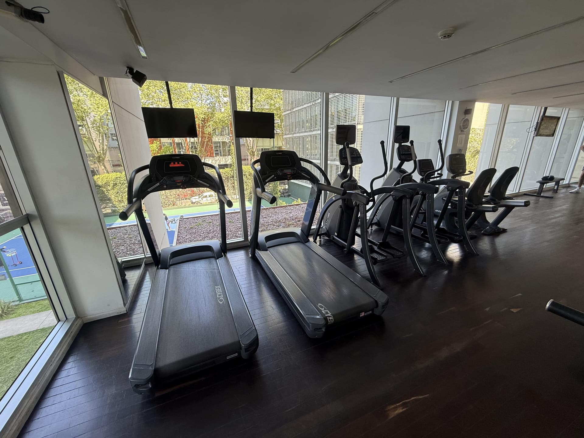 Gimnasio con máquinas caminadoras, elípticas y pantallas.