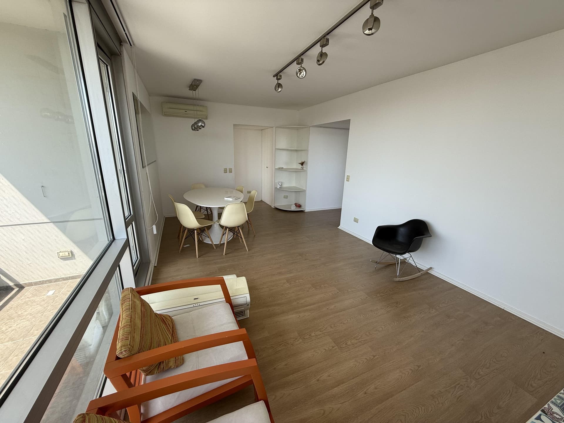 Living con mesa de comedor blanca, sillones y amplios ventanales.