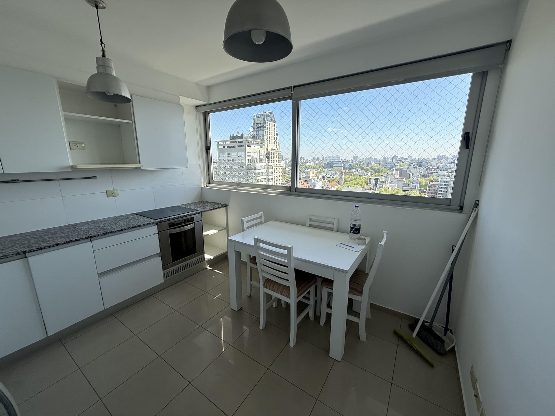 Cocina con mesada, horno, alacenas blancas y mesa con sillas.