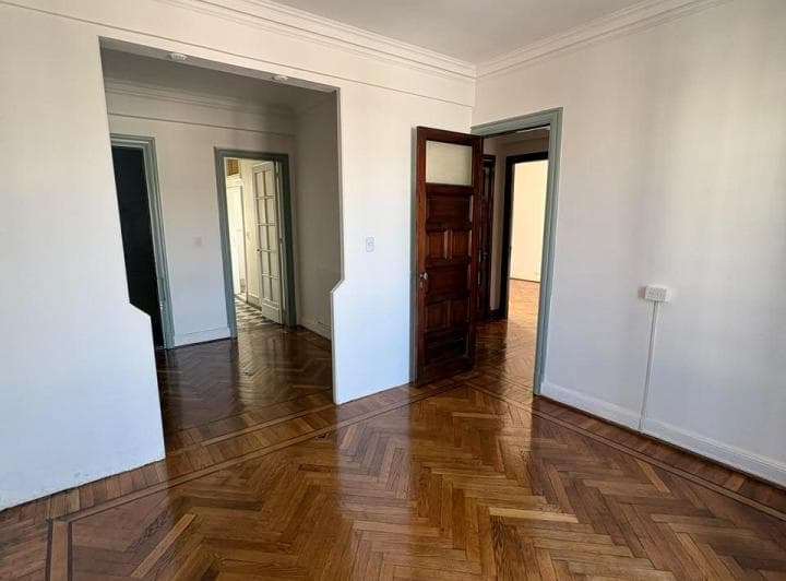 Living vacío con piso de parquet y varias puertas de madera.