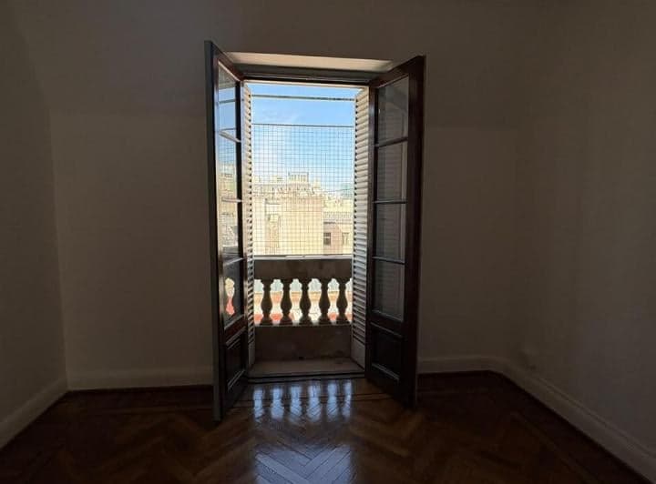 Living vacío con puerta balcón abierta a la ciudad, piso de parquet.