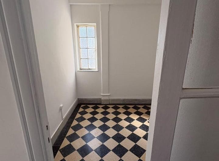 Dormitorio vacío con piso de baldosas blancas y negras, ventana pequeña.