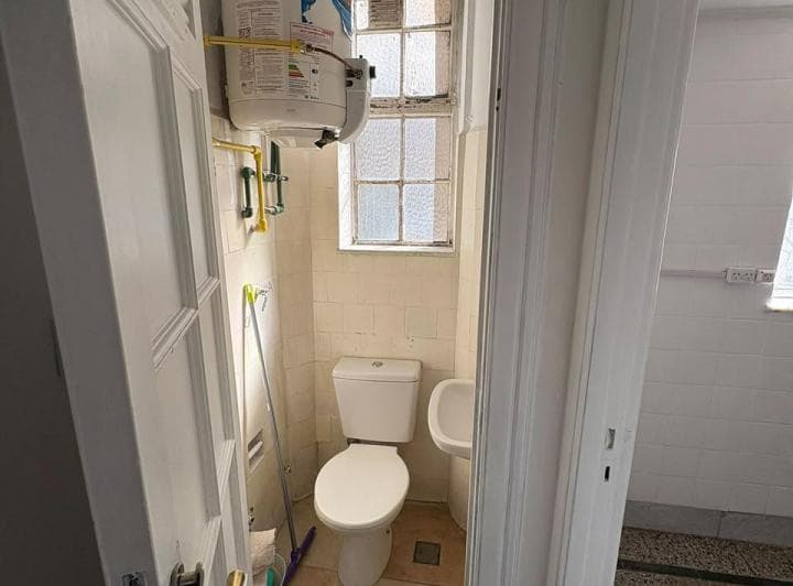 Toilette con inodoro, lavatorio y termotanque, azulejos claros.