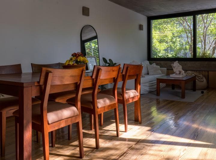 Living comedor con mesa de madera, sillas, espejo y sillón blanco.