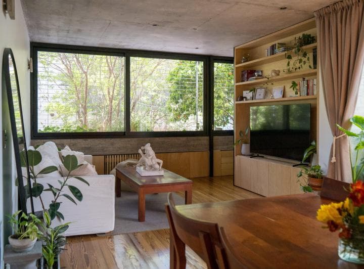 Living con sillón blanco, mesa ratona, televisor y estantería de madera.