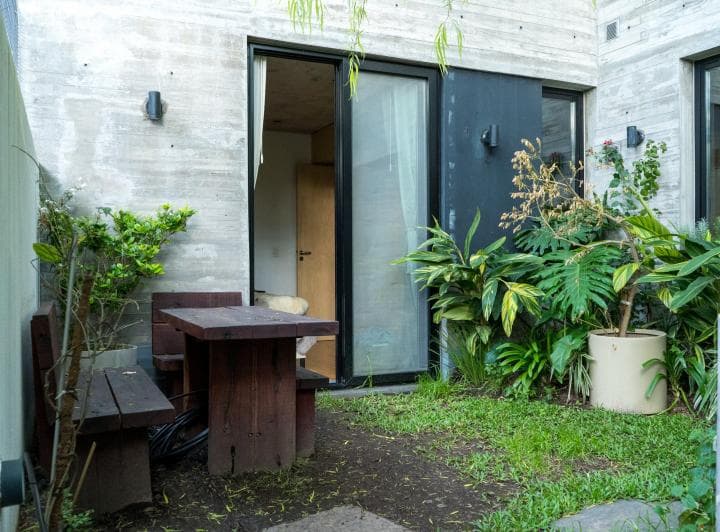 Patio con jardín, mesa de madera con bancos y plantas en macetas.