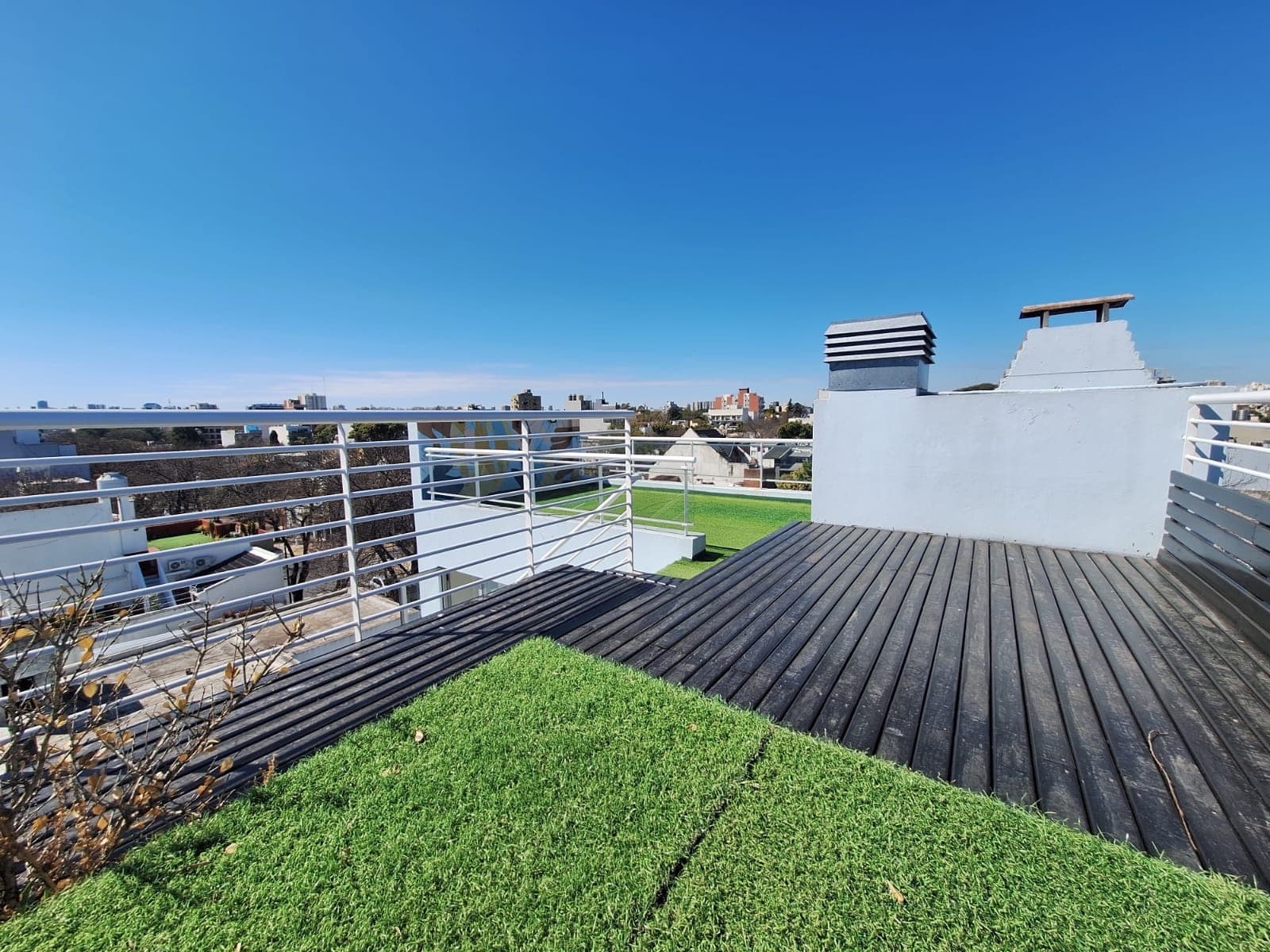 Balcón terraza con piso de madera, césped artificial y vista urbana.