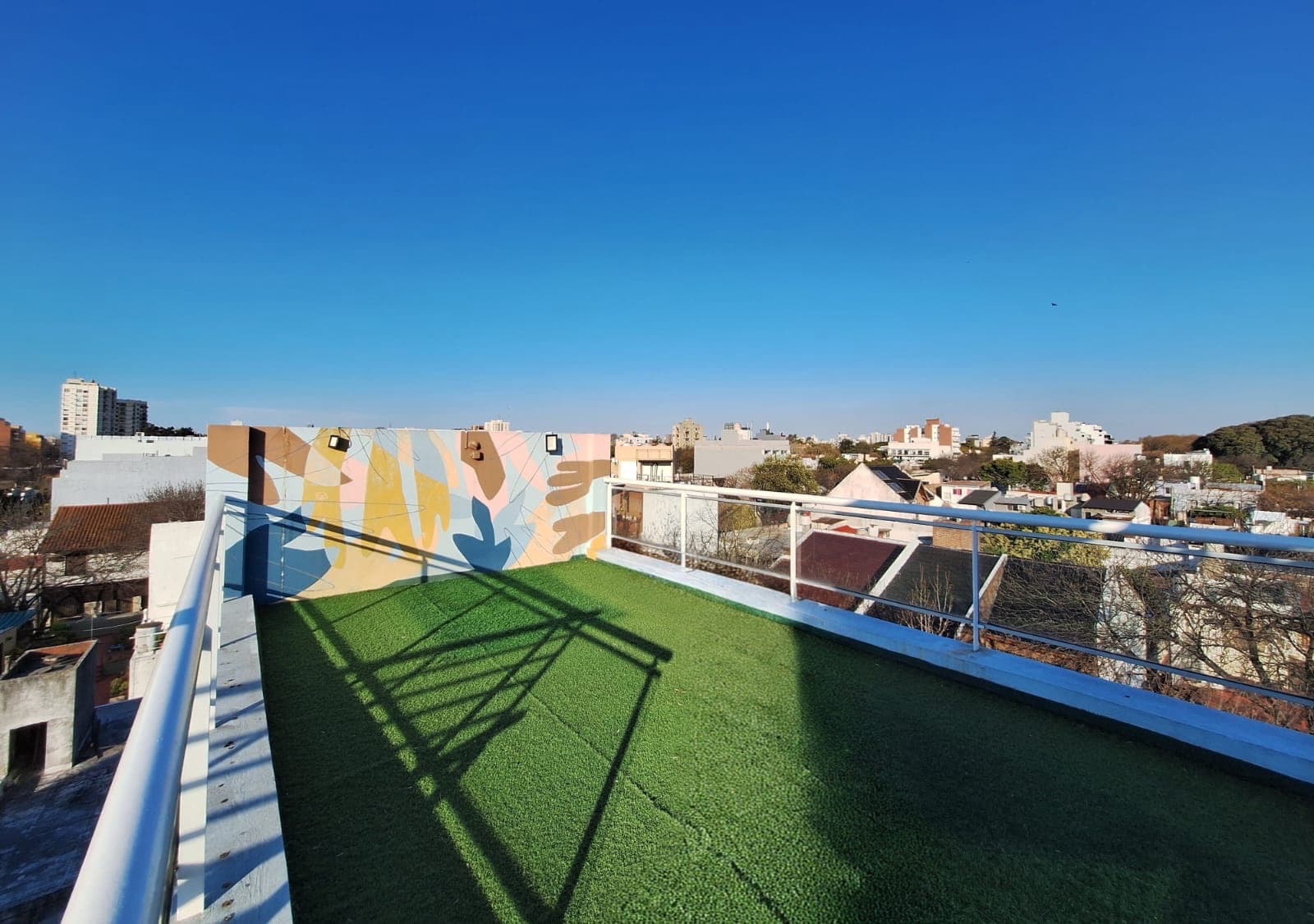 Balcón terraza con césped artificial, mural y vista a la ciudad.